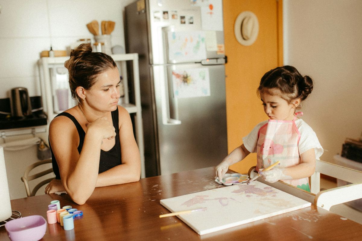 A mother at the kitchen table watching her little girl paint