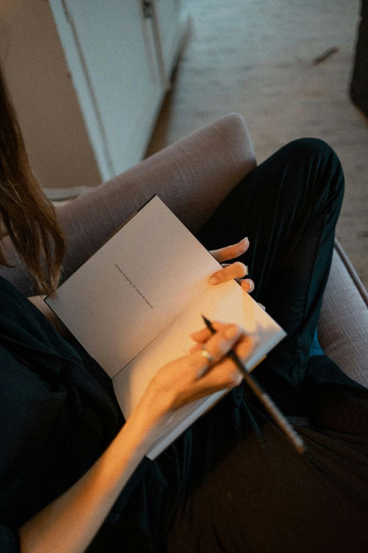 A woman's hands writing in a notebook on her lap